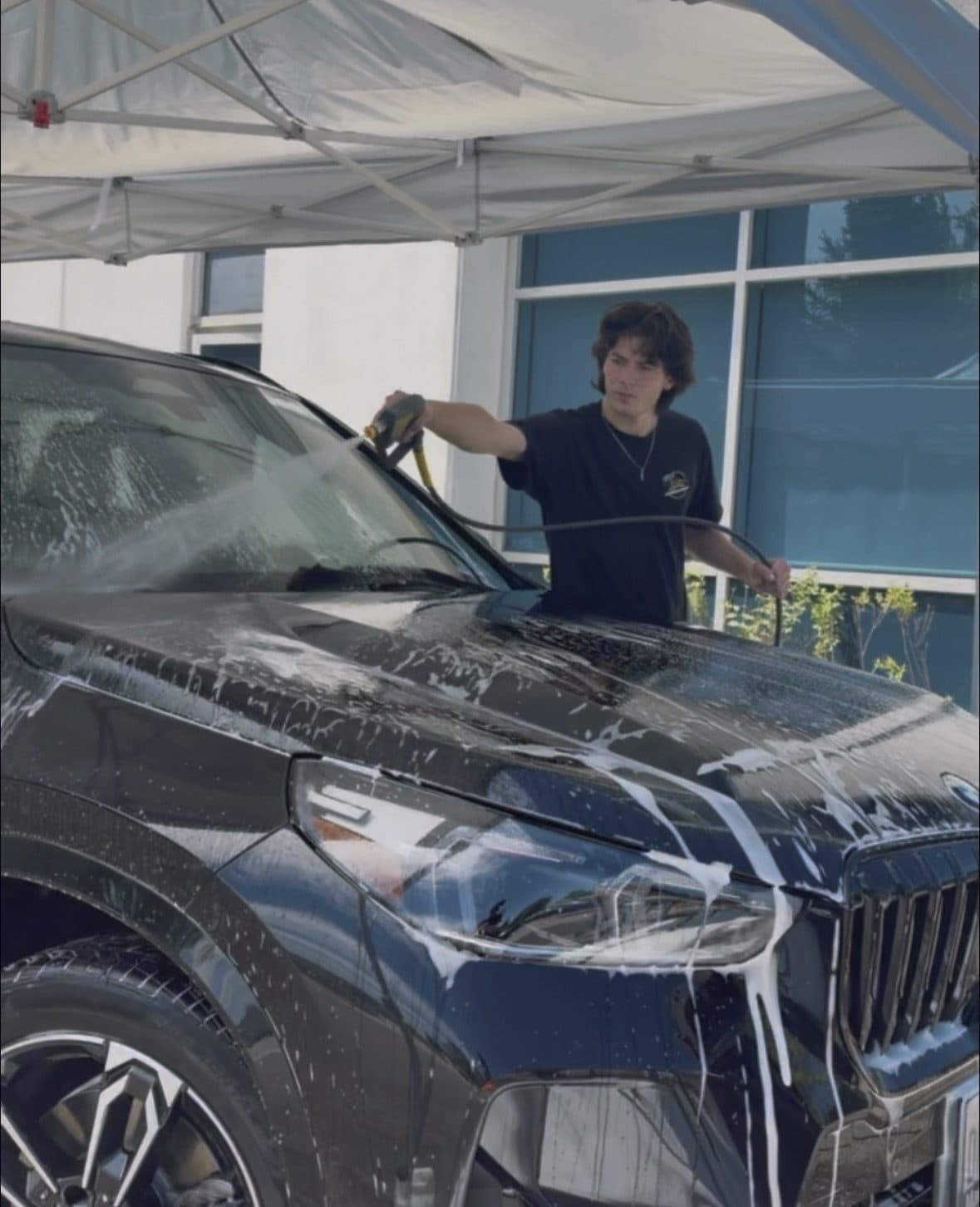 Technician foaming and rinsing a black BMW SUV during a Silver Exterior wash